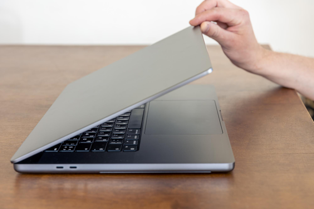 Hand lifting the lid of a silver laptop on a wooden desk
